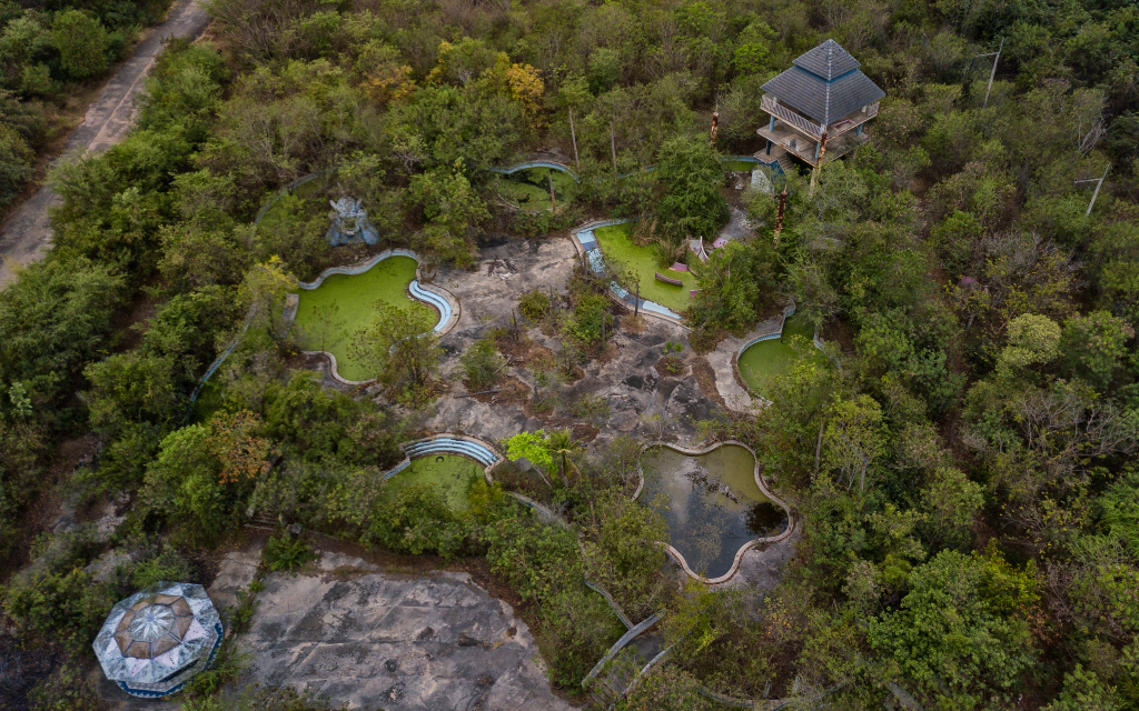 Aerial view of the abandoned Castle Mall amusement park, overgrown with trees and several empty, mossy pools.