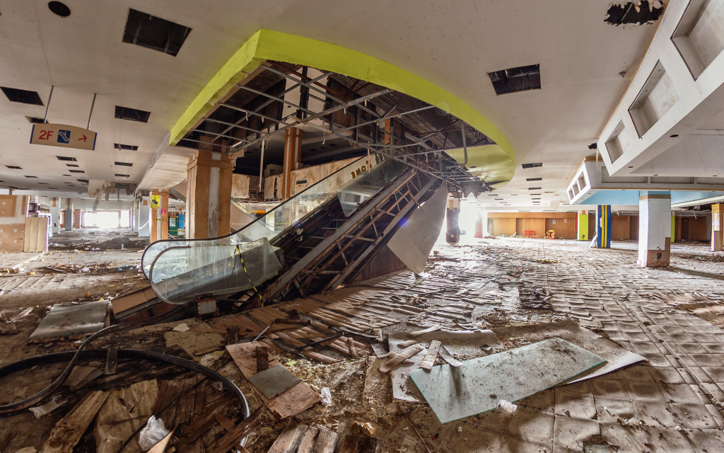 An abandoned mall with a destroyed escalator and debris scattered on the floor.