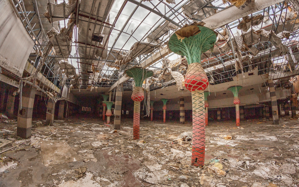 The derelict interior of Castle Mall entertainment park, with palm tree shaped pillars and a damaged ceiling.