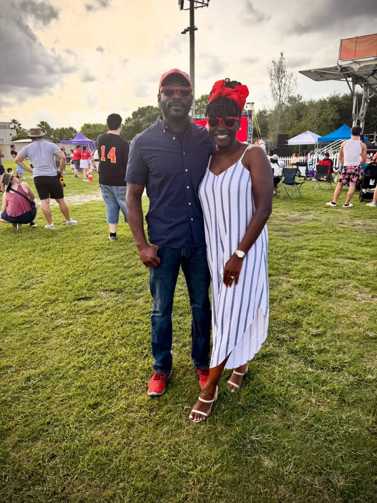 A man and woman standing on grass, smiling, at an outdoor event.