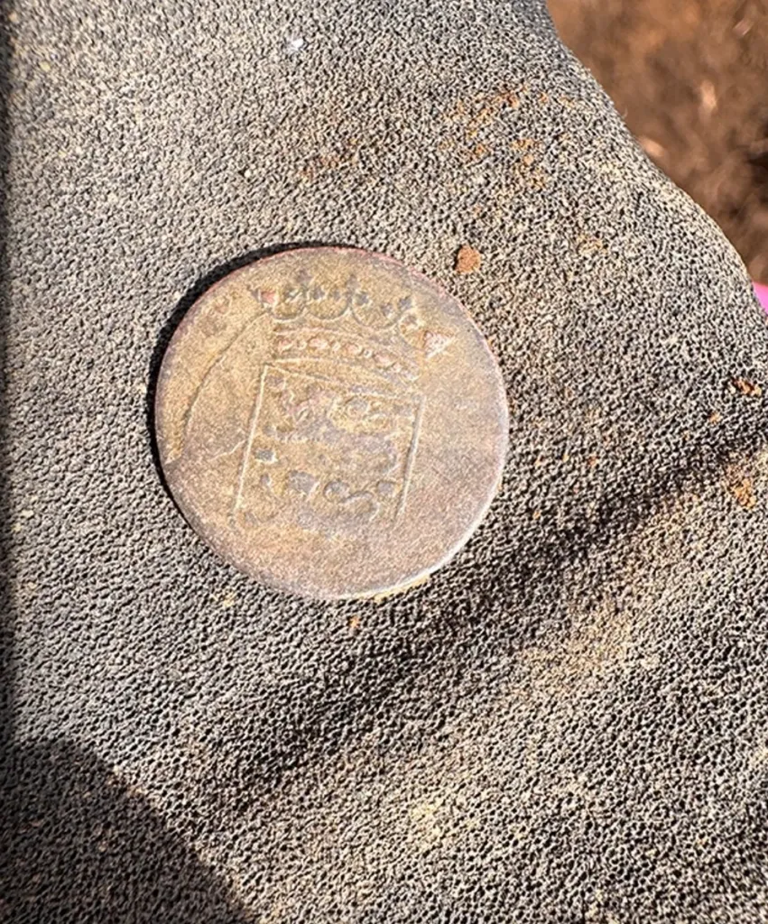 A colonial-era coin with a crowned crest design found at an archaeological dig.