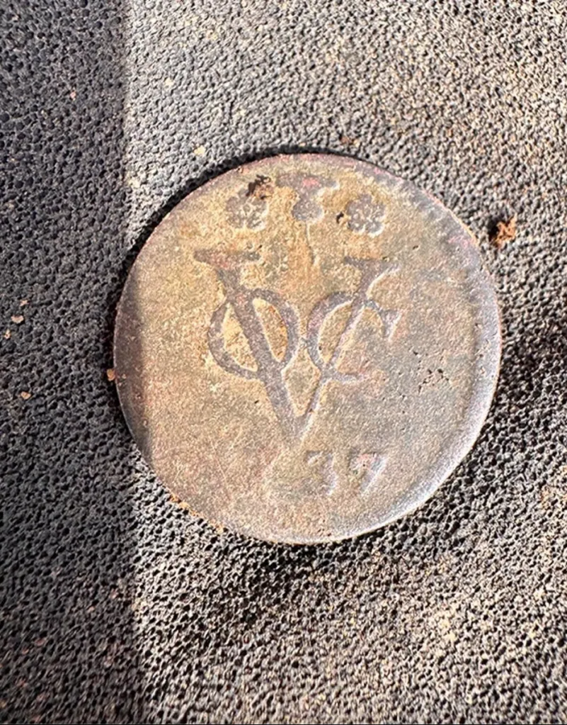 Close-up of an unearthed colonial-era coin with the letters 