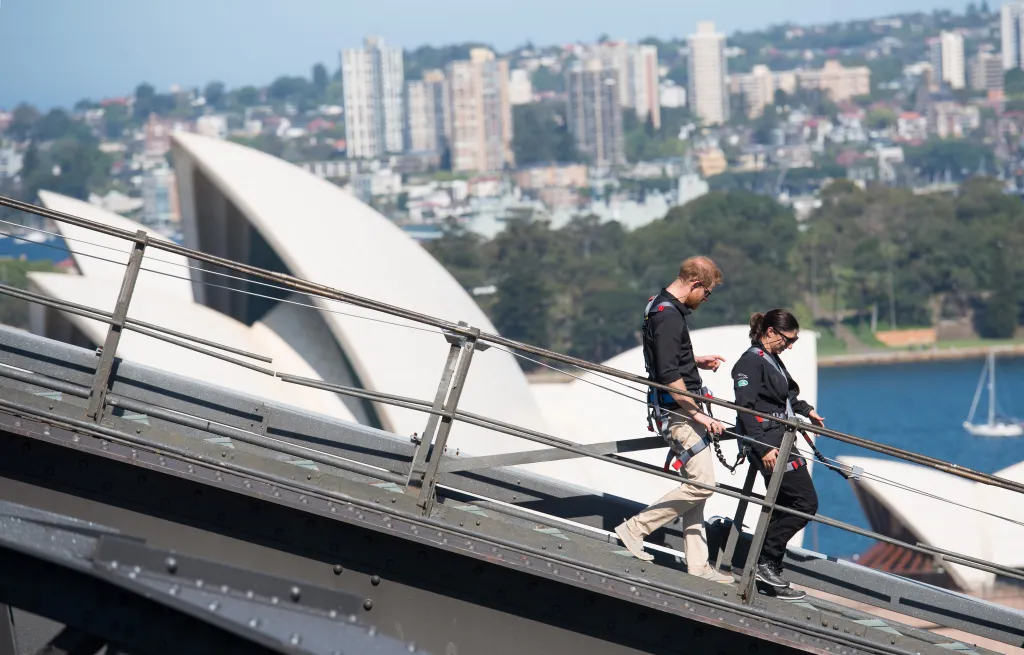 Prince Harry, in a blue shirt and khaki pants, and an Invictus Games competitor climbing the Sydney Harbour Bridge.