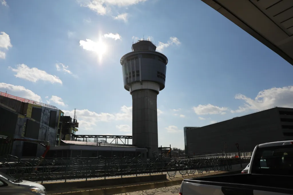 LaGuardia Airport's control tower with a sun flare and clouds above.