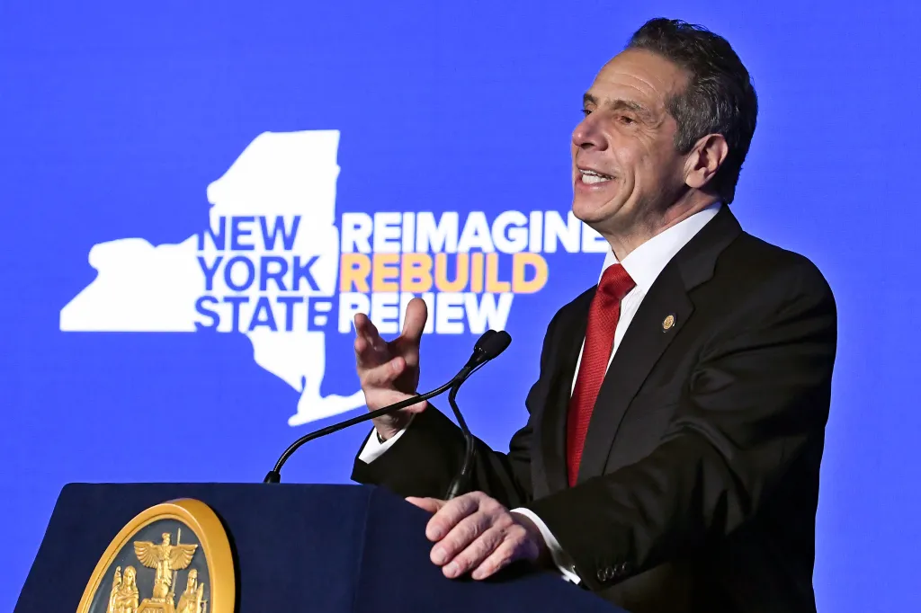 New York Gov. Andrew Cuomo speaks at a podium with a blue screen behind him displaying the words 