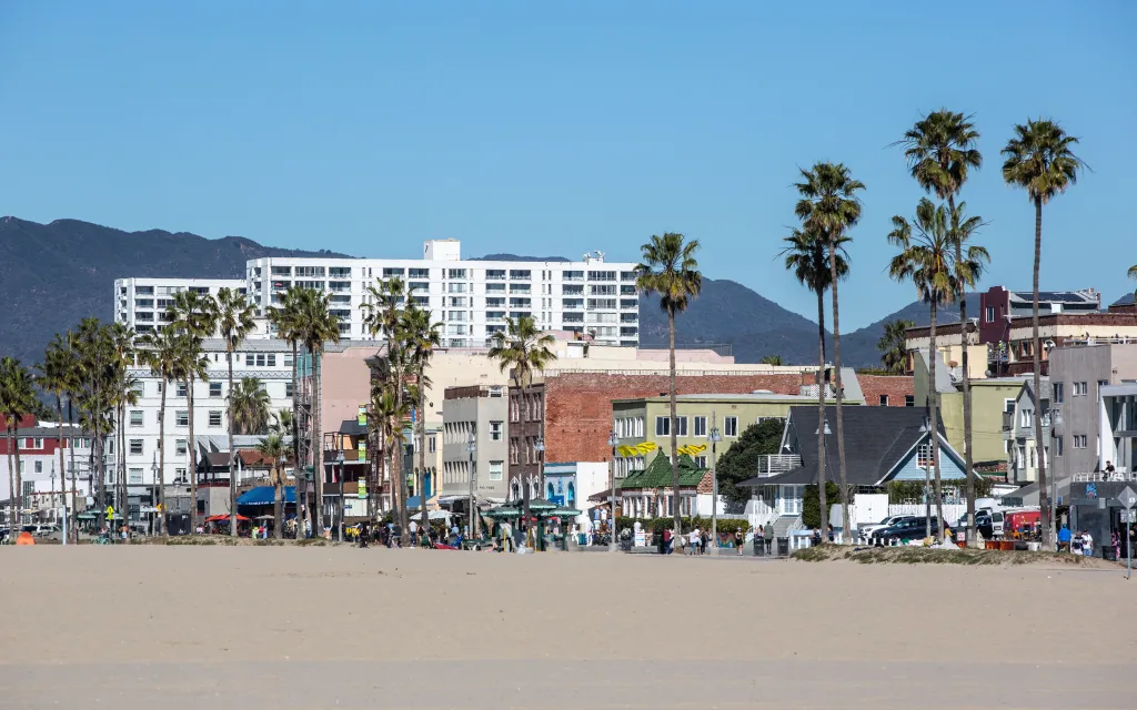 The boardwalk and buildings of Venice Beach, California with mountains in the background.