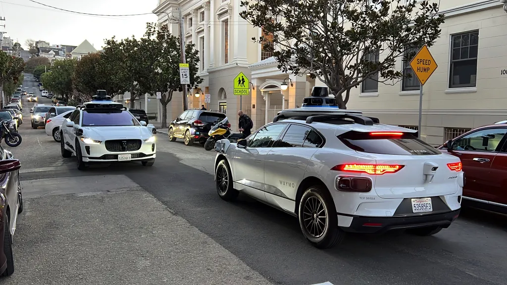 Two Waymo driverless taxis stop and face each other on a street in San Francisco.