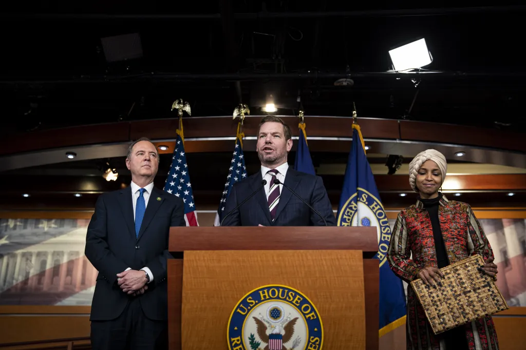 Representative Eric Swalwell speaks at a news conference while Representative Adam Schiff and Representative Ilhan Omar stand beside him.