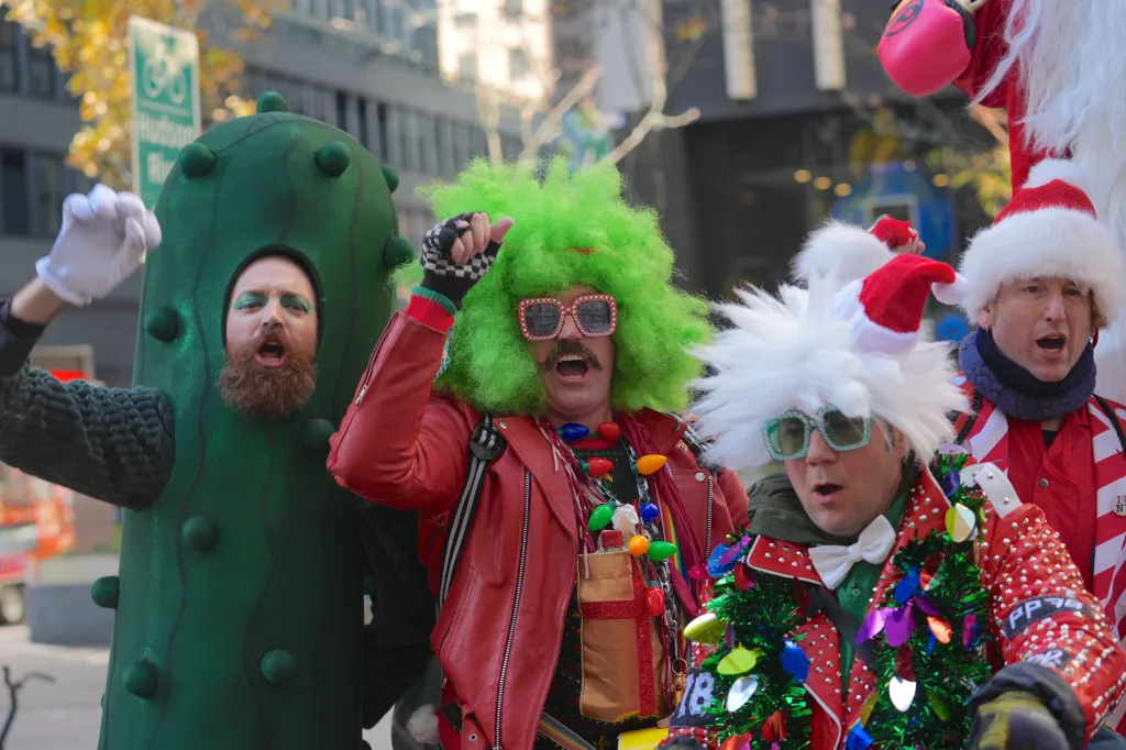 Four participants at SantaCon 2024, including one dressed as a pickle, and another with a bright green wig, mustache, and light-up necklace.