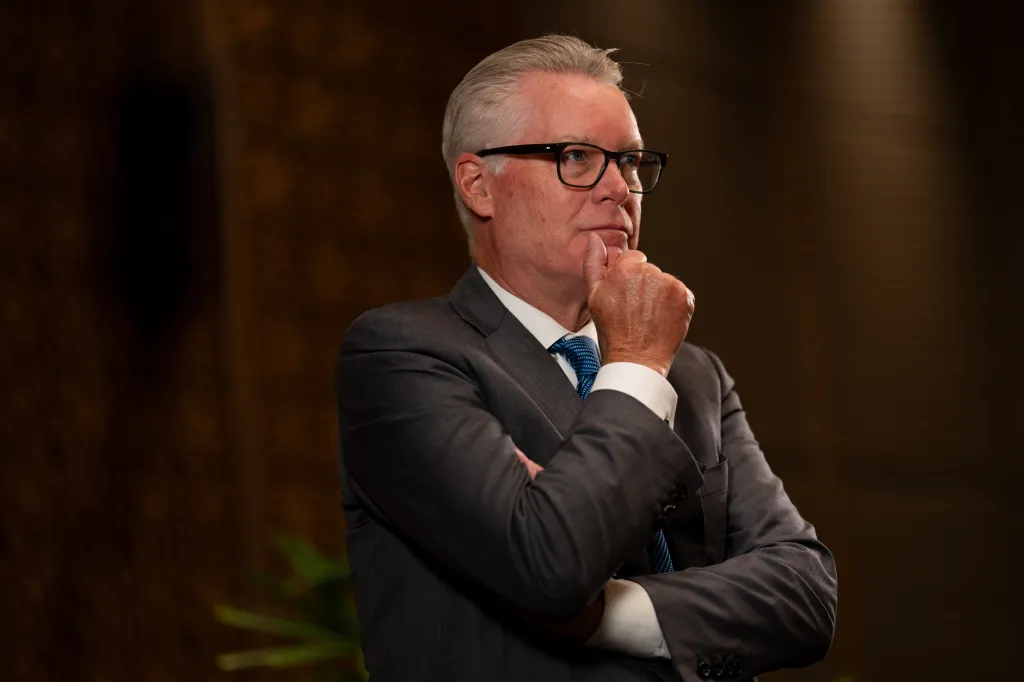 Ed Bastian, CEO of Delta Air Lines, wearing glasses and a suit, with his hand on his chin, looking contemplatively to the right.