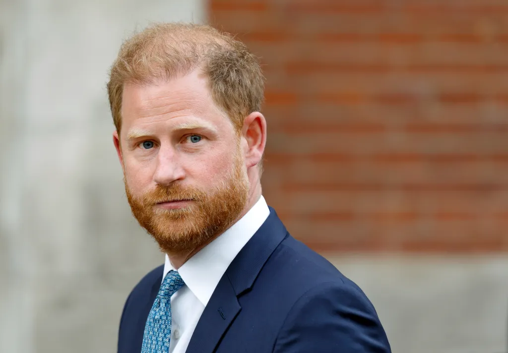 Prince Harry, Duke of Sussex, wearing a blue suit and patterned blue tie, looks at the camera.
