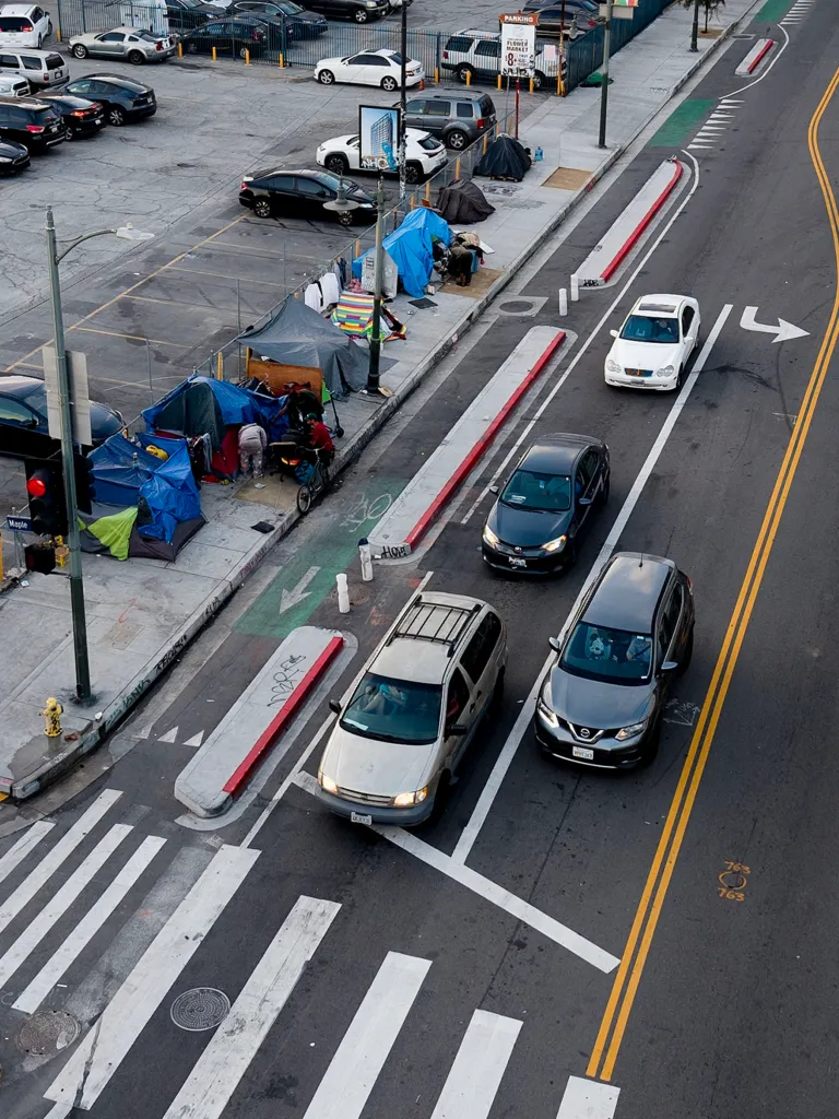 Homeless encampments in Downtown Los Angeles, with tents and belongings lining the sidewalk next to a busy street.