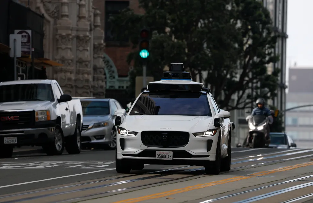 A white Waymo robotaxi drives along California Street in San Francisco.