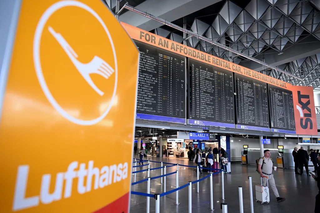 Lufthansa logo in an airport terminal with a departures board in the background showing many cancelled flights.