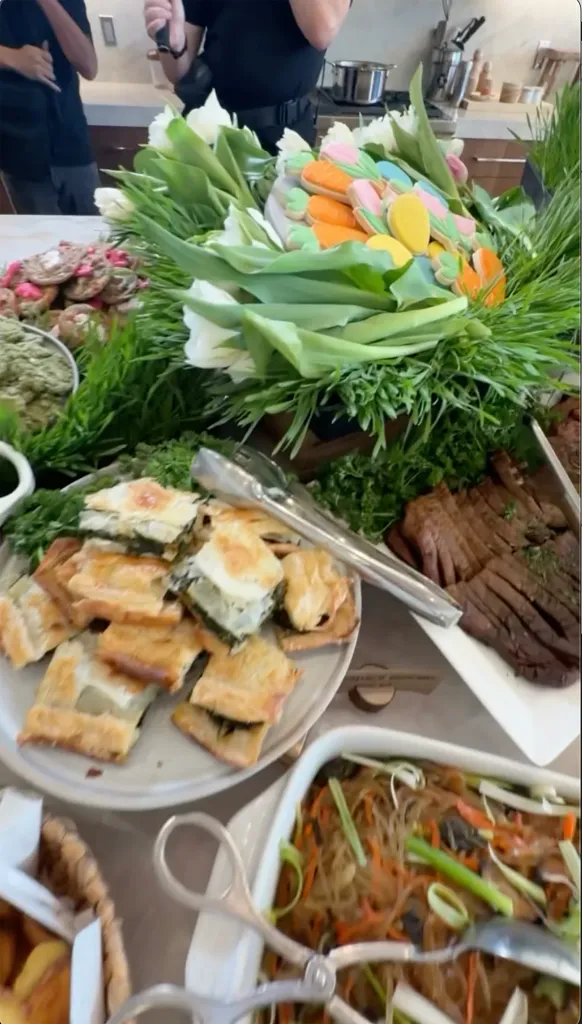 Table set for an Easter brunch, including pastries, sliced meat, noodles, and festive cookies in the shape of carrots and eggs.