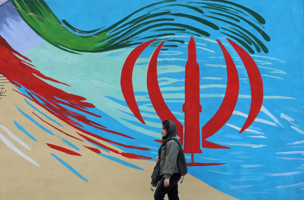 An Iranian woman walking in front of a wall mural of the Iranian national flag.