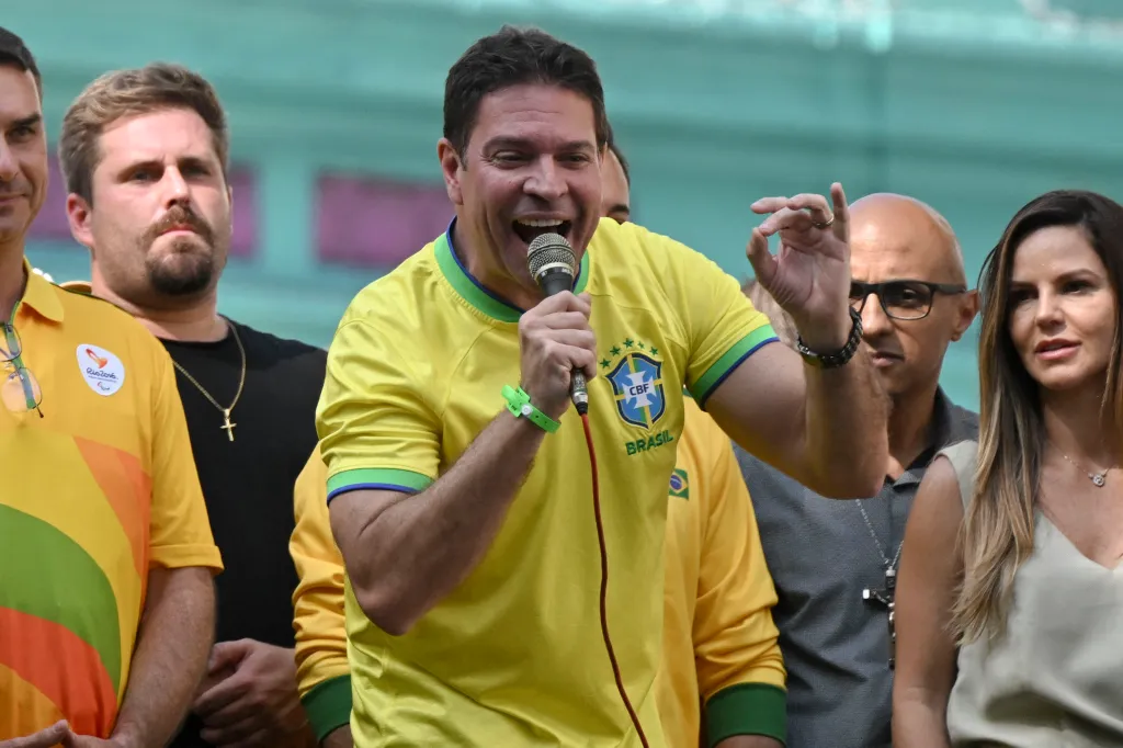 Brazilian politician Alexandre Ramagem speaks into a microphone while wearing a yellow Brasil soccer jersey.