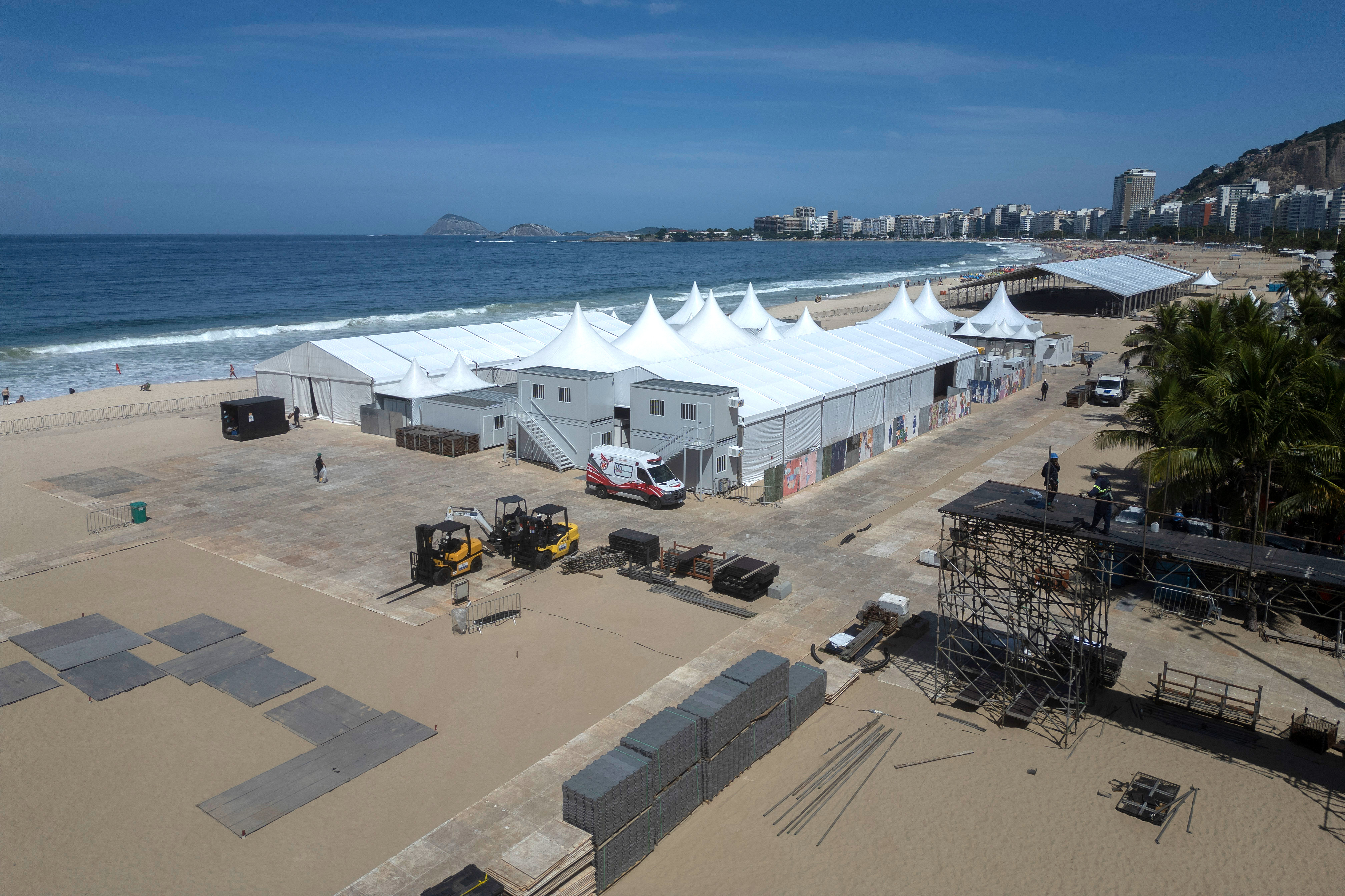 Aerial view of the stage setup for Shakira's concert at Copacabana Beach in Rio de Janeiro, with numerous white tents and a partially constructed stage.