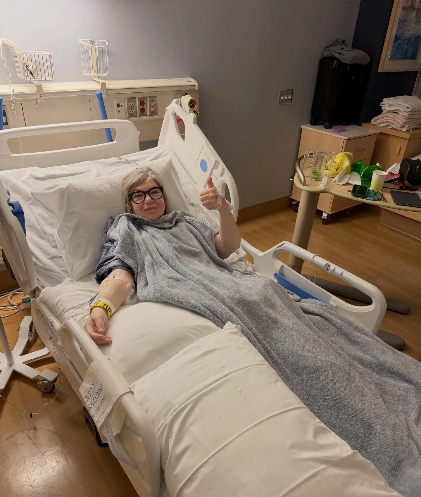 Mindy Cohn gives a thumbs up while lying in a hospital bed.