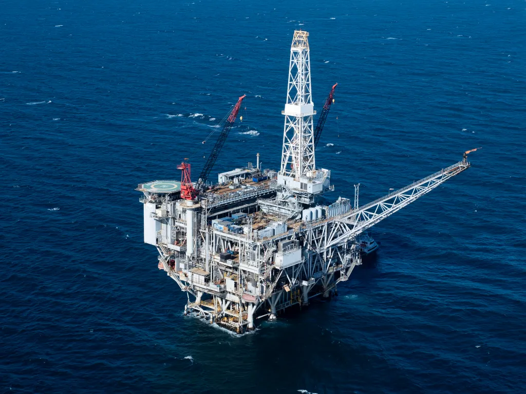 An aerial view of the Sable Offshore Heritage platform, an oil rig with a helipad and a flare burning, surrounded by blue ocean.