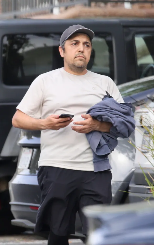 Eissa Hashemi in a light t-shirt and dark shorts, holding a phone and a jacket, in front of a dark car.