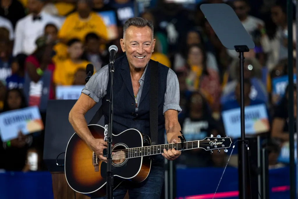 Bruce Springsteen performing with an acoustic guitar at a campaign event.