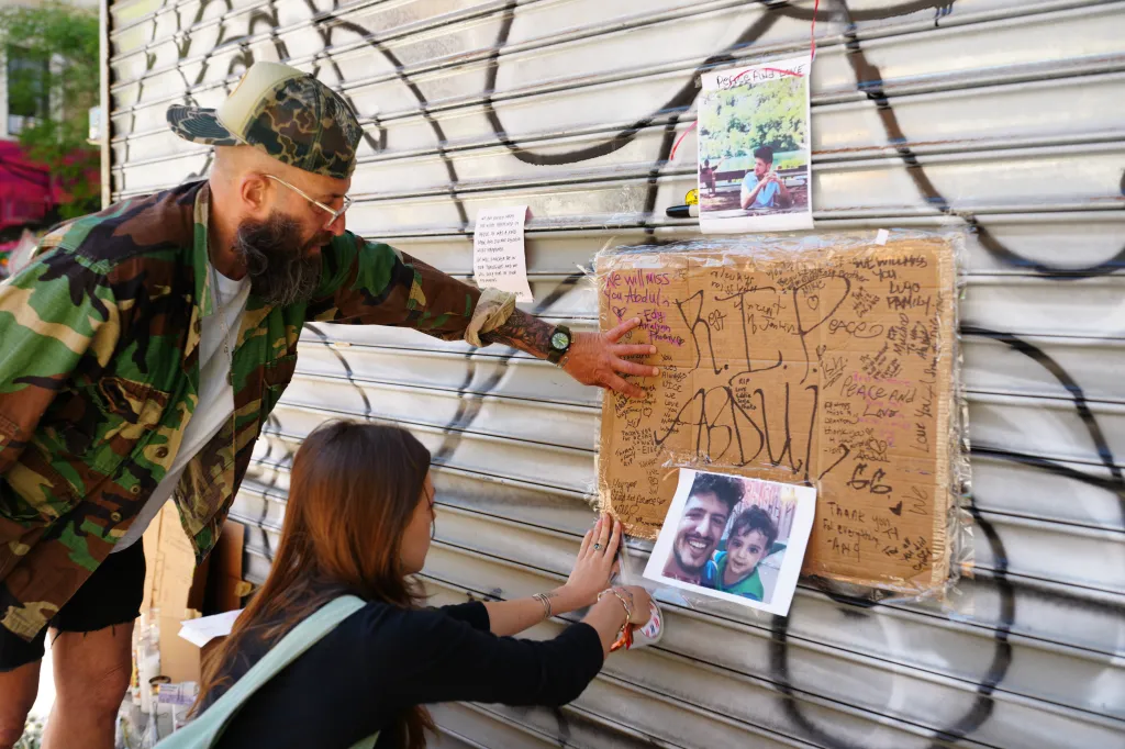 Mia Safanda and Vito DiTomaso placing signs and photos at a memorial outside Sal’s Deli & Grocery.