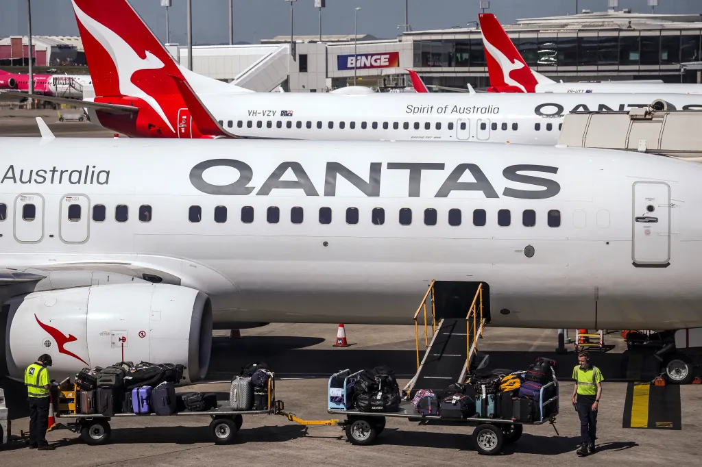 Ground staff loading luggage onto a Qantas Airways Boeing 737 aircraft at an airport.