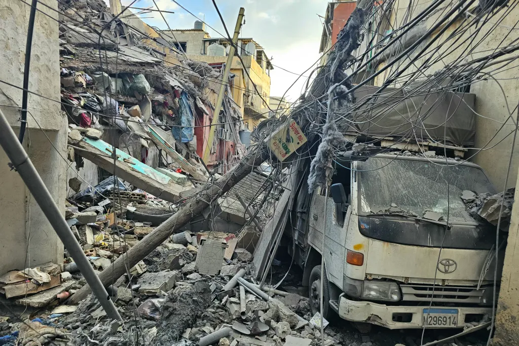 The aftermath of an Israeli airstrike in southern Beirut's al-Rihab neighborhood, showing a damaged white truck surrounded by debris and collapsed buildings.