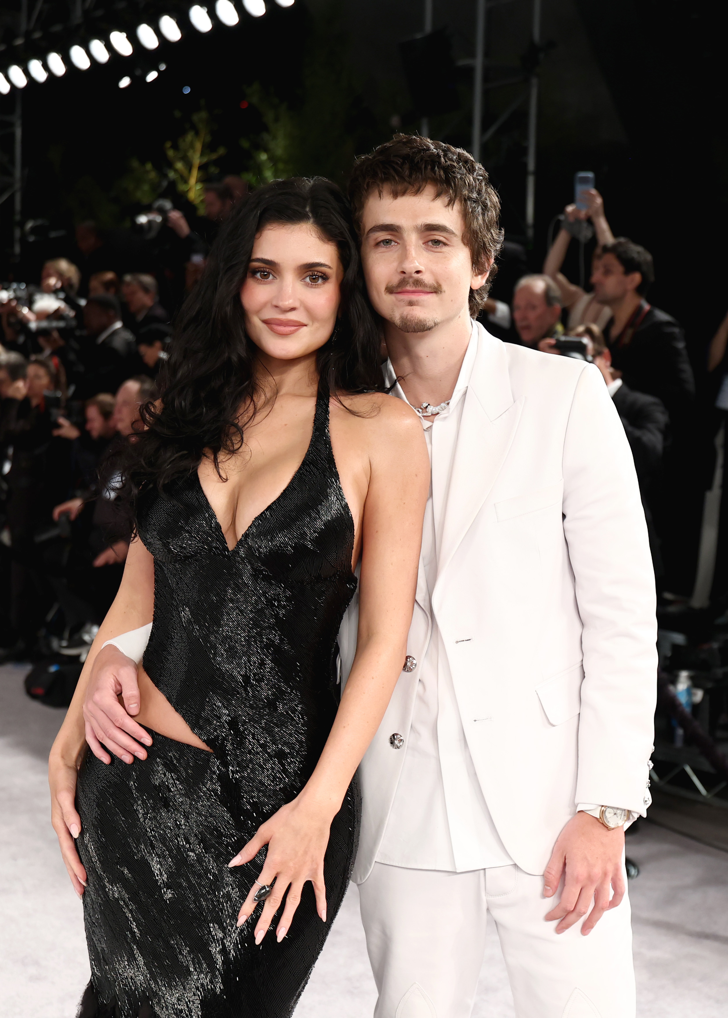 Kylie Jenner in a black sequined dress and Timothée Chalamet in a white suit pose for a photo.