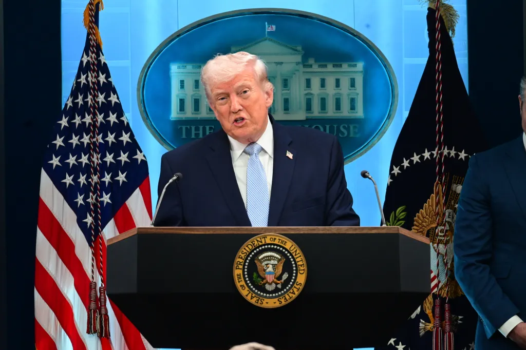 President Trump speaks from a podium with the Seal of the President on it, flanked by American flags and a White House backdrop.
