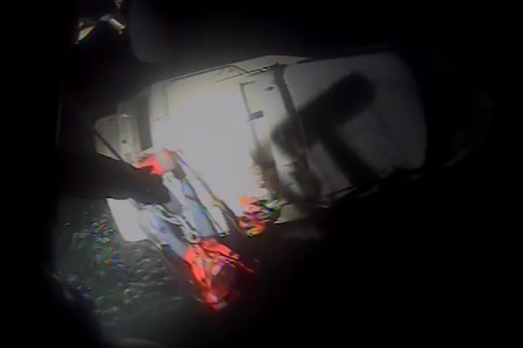 A Coast Guard crew member helping rescue a person from a disabled motor yacht at night.