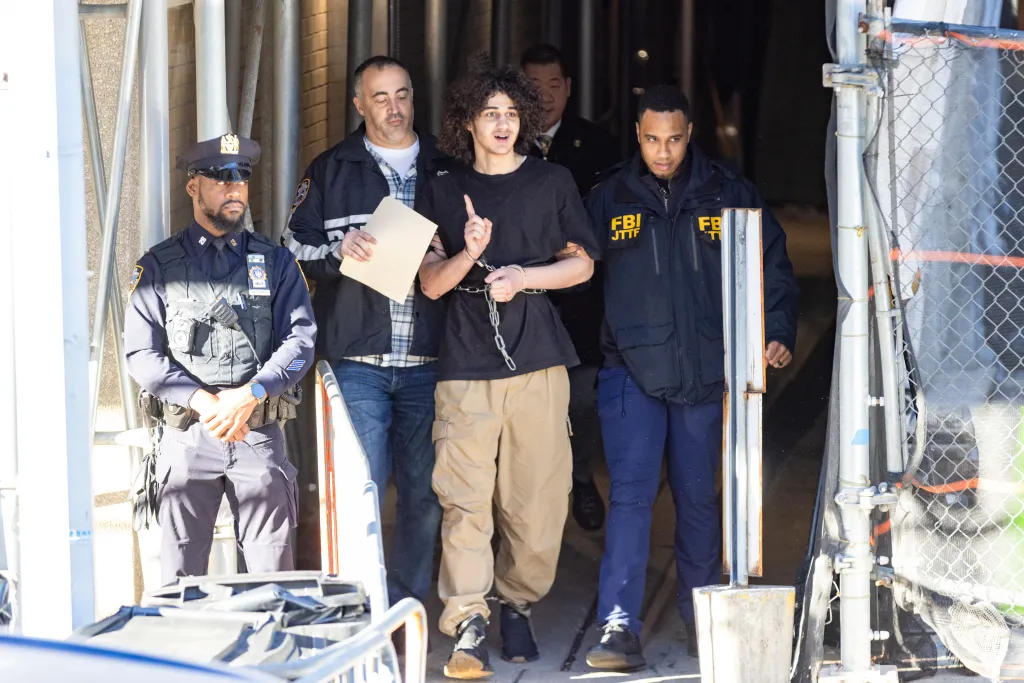 A man in handcuffs and chains being escorted by law enforcement officials.