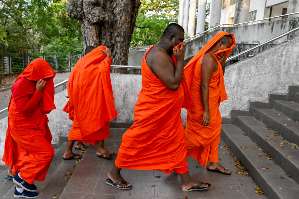 Buddhist monks in orange robes covering their faces as they walk up stairs.