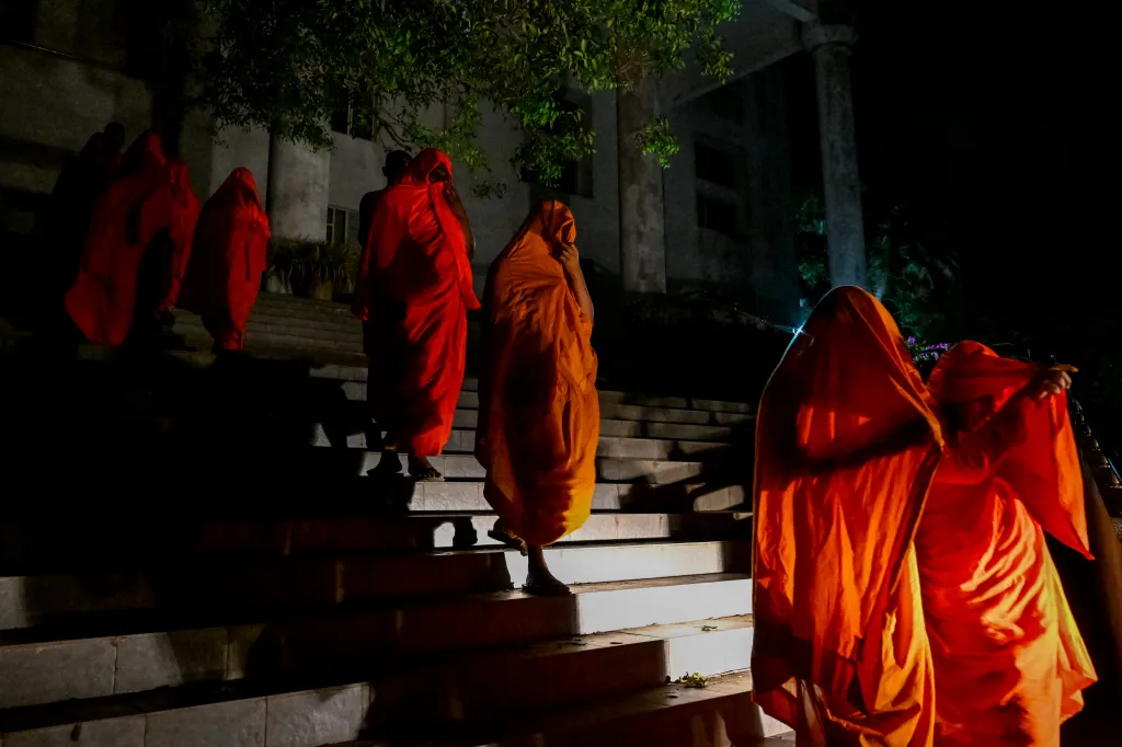 Monks in orange robes ascending stairs at night.