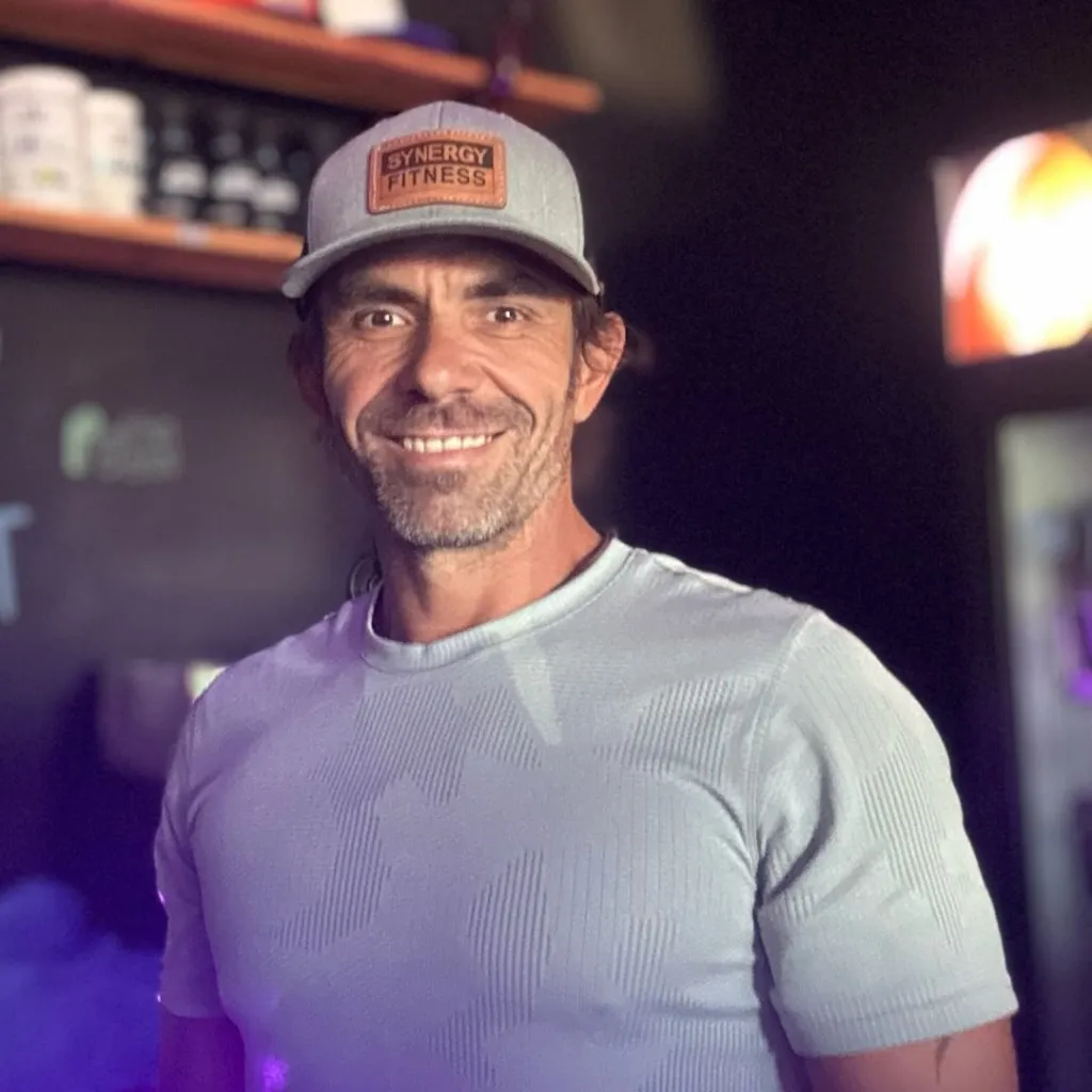 Joshua Swalwell smiling and wearing a grey Synergy Fitness cap and a light blue shirt.