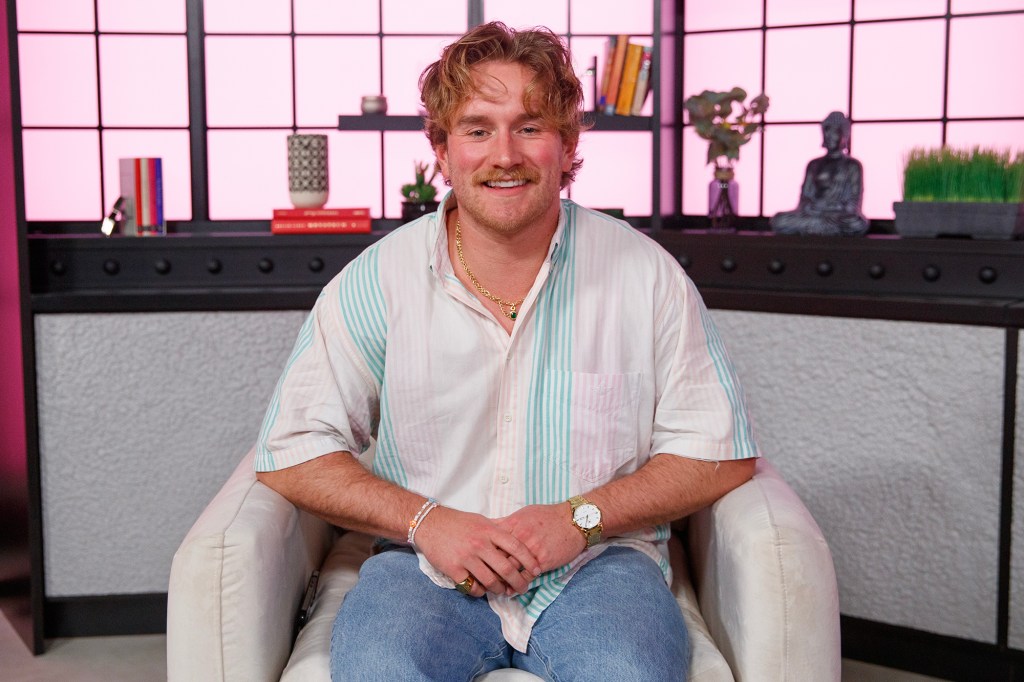 West Wilson of Summer House Season 8 sitting in a chair, wearing a striped shirt and jeans, for a Page Six interview.