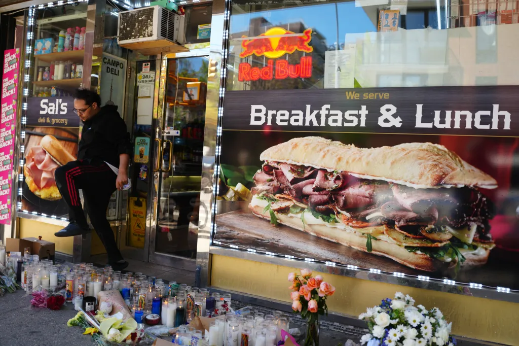 A man walks past a makeshift memorial of candles and flowers outside Sal's Deli & Grocery.