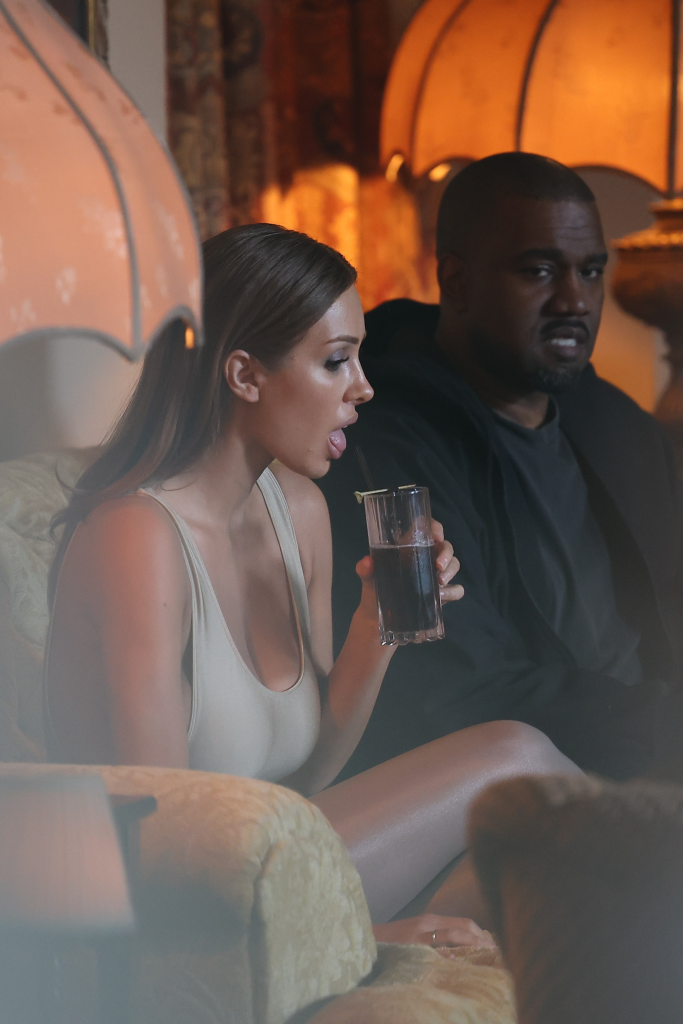 Bianca Censori drinking from a glass next to Kanye West in a dimly lit room.
