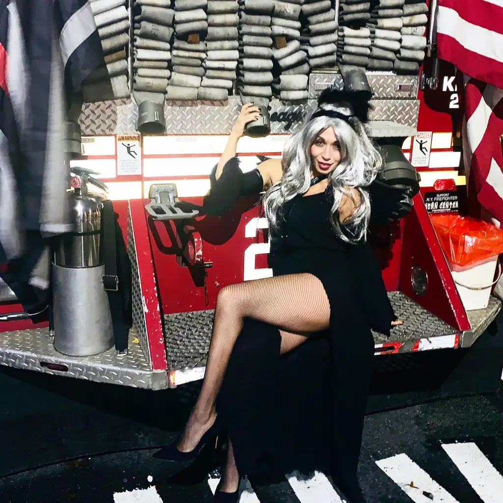 A woman with long white hair posing on the back of a red FDNY fire truck.