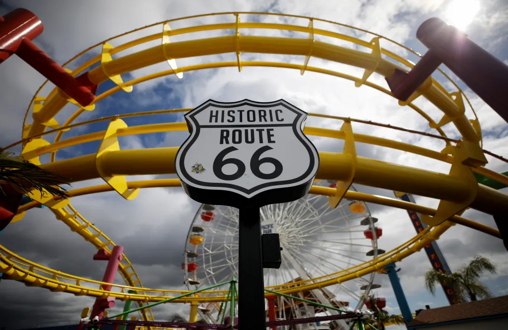Historic Route 66 sign in front of a closed roller coaster and Ferris wheel at Santa Monica Pier.