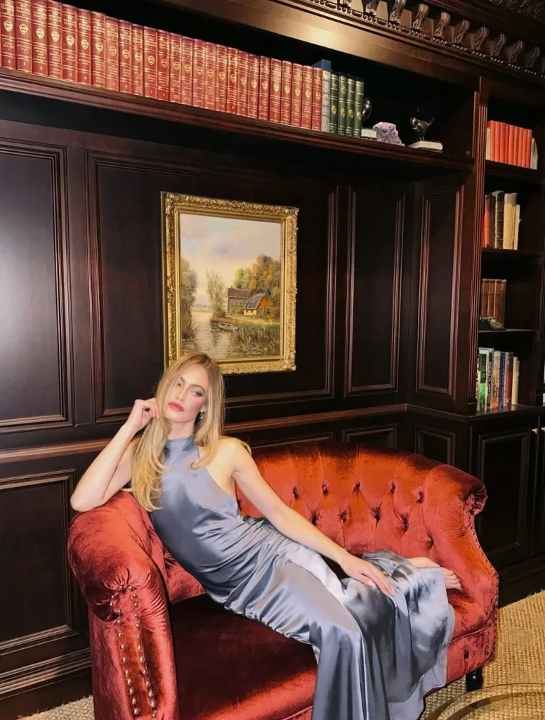 Hailey Carlson in a blue dress sitting on a red couch in a library.