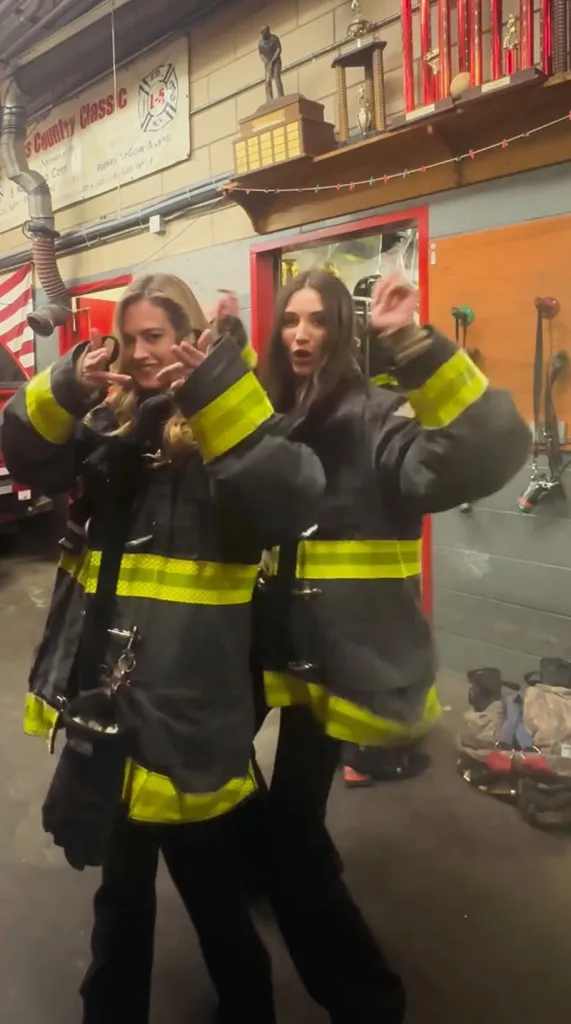 Two women dancing in firefighter gear inside a fire station.