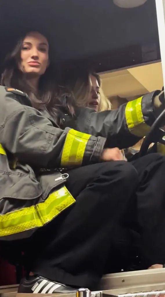 Dana Treacy and Hailey Carlson dancing in a fire truck while wearing firefighter uniforms.