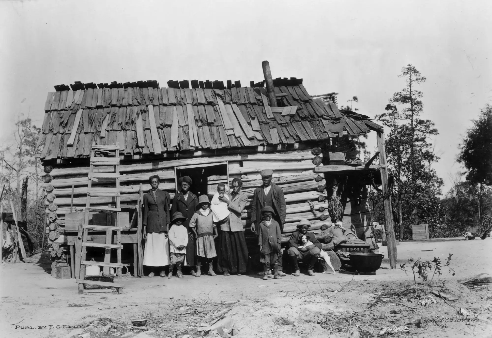 An African-American family during the Great Depression poses in front of a log cabin.