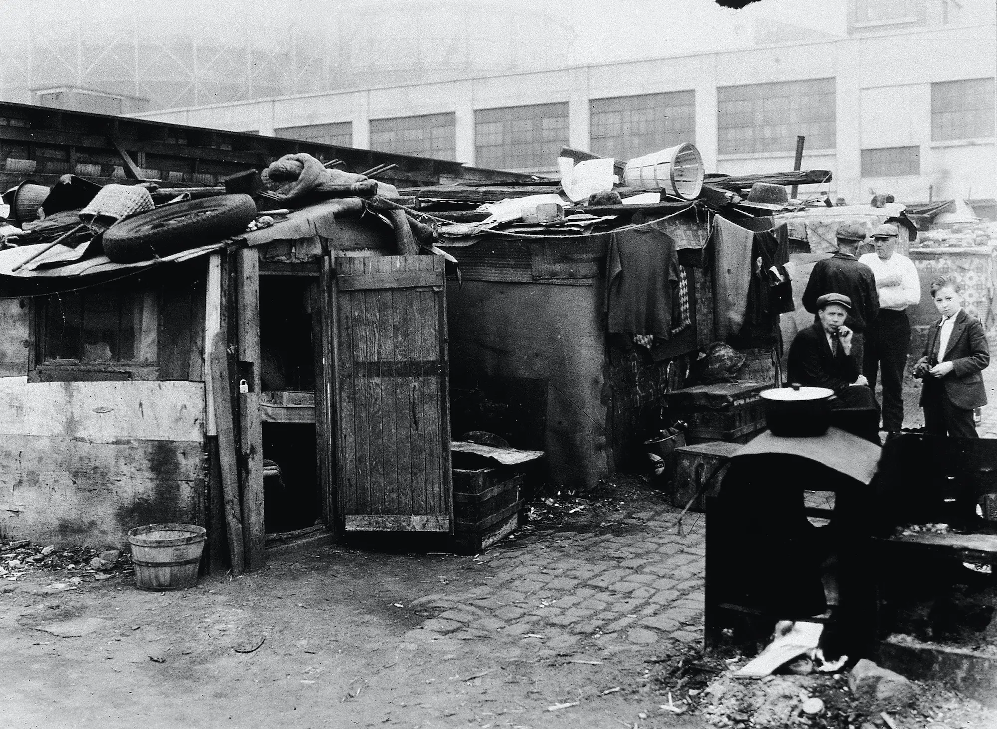 A group of men and a boy standing outside a shack in a shantytown in the 1930s.