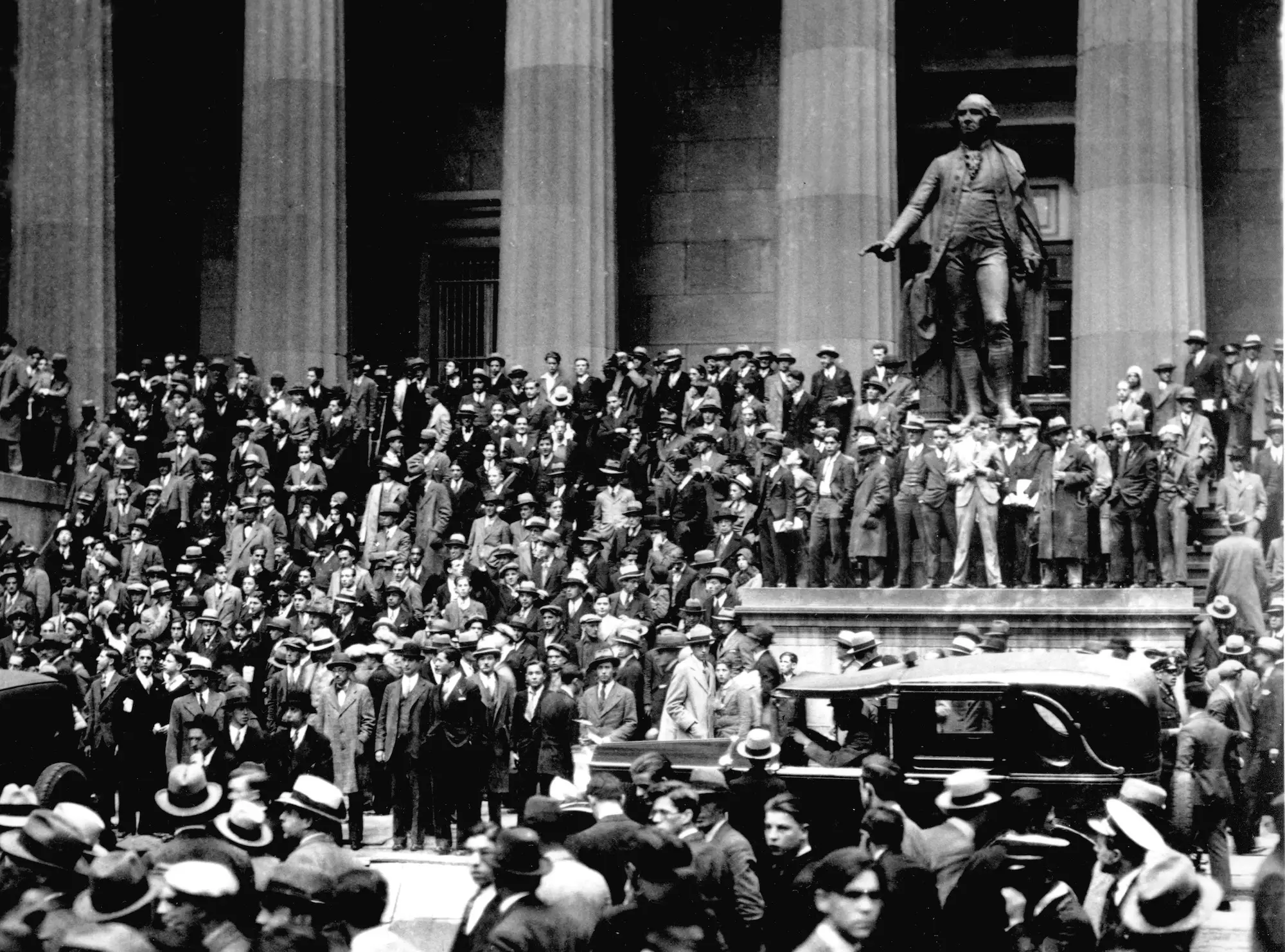 A crowd of men in suits and coats are seen outside the New York Stock Exchange in a black and white photo