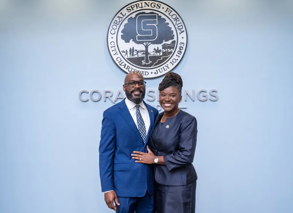 A man and woman smiling in front of the Coral Springs, Florida city seal.