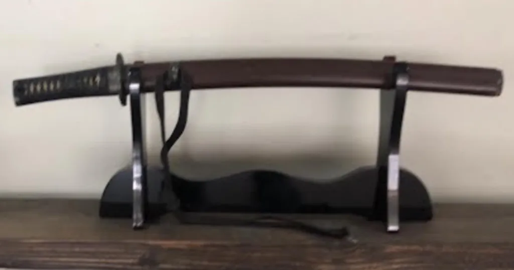 Historic samurai sword with a dark brown sheath resting on a black stand.