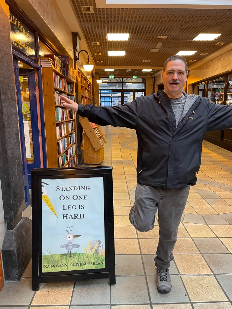 A man balances on one leg next to a sign that reads 